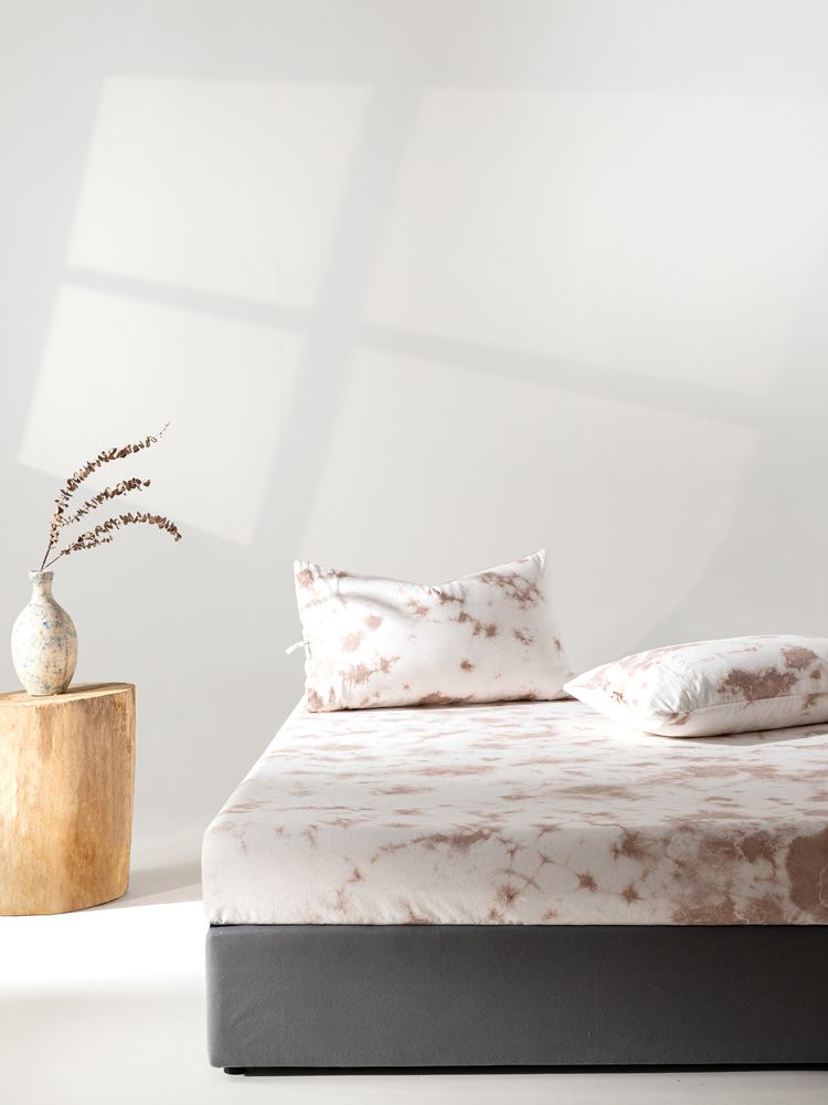 Walnut husk dyed linen-cotton fitted sheet on a bed